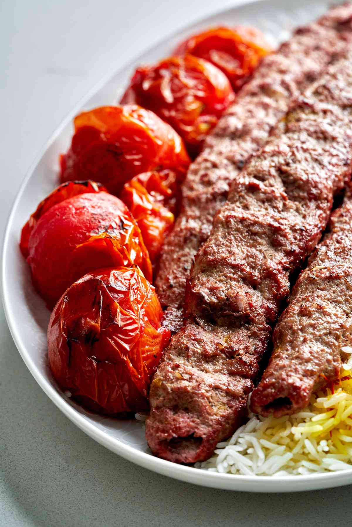 Meat kabobs on a plate with tomatoes.
