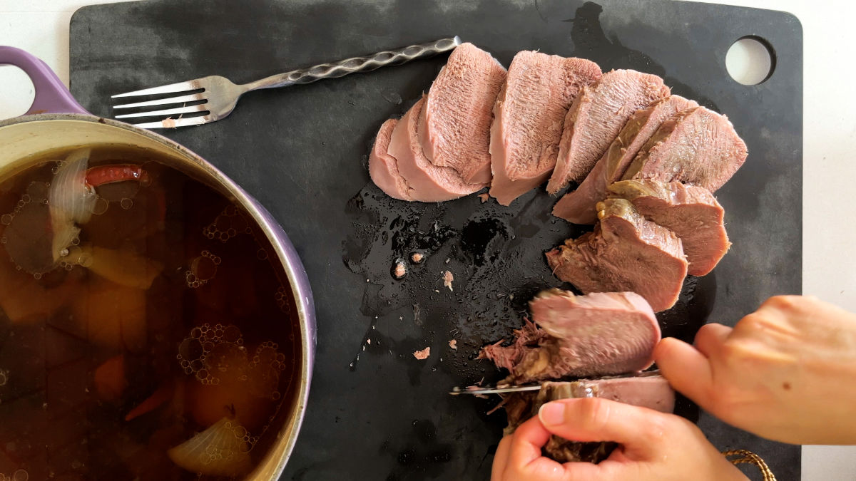 Slicing beef tongue on a black cutting board.