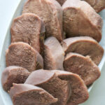 Top view of sliced cow tongue on a plate.