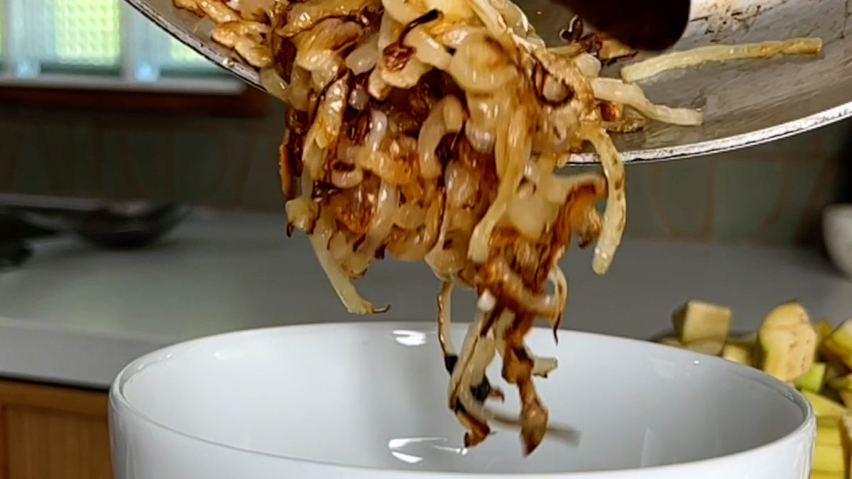 Fried onions being poured from a pan to a bowl.