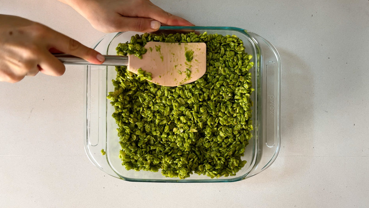 Spatula pressing green rice crispy into a baking dish.