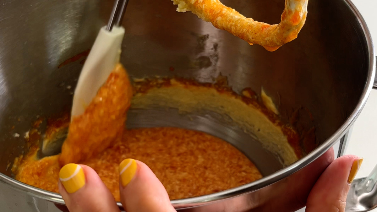 Scraping the sides of a metal bowl with a rubber spatula.