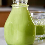 Milk jug filled with Matcha Baileys next to a cocktail.