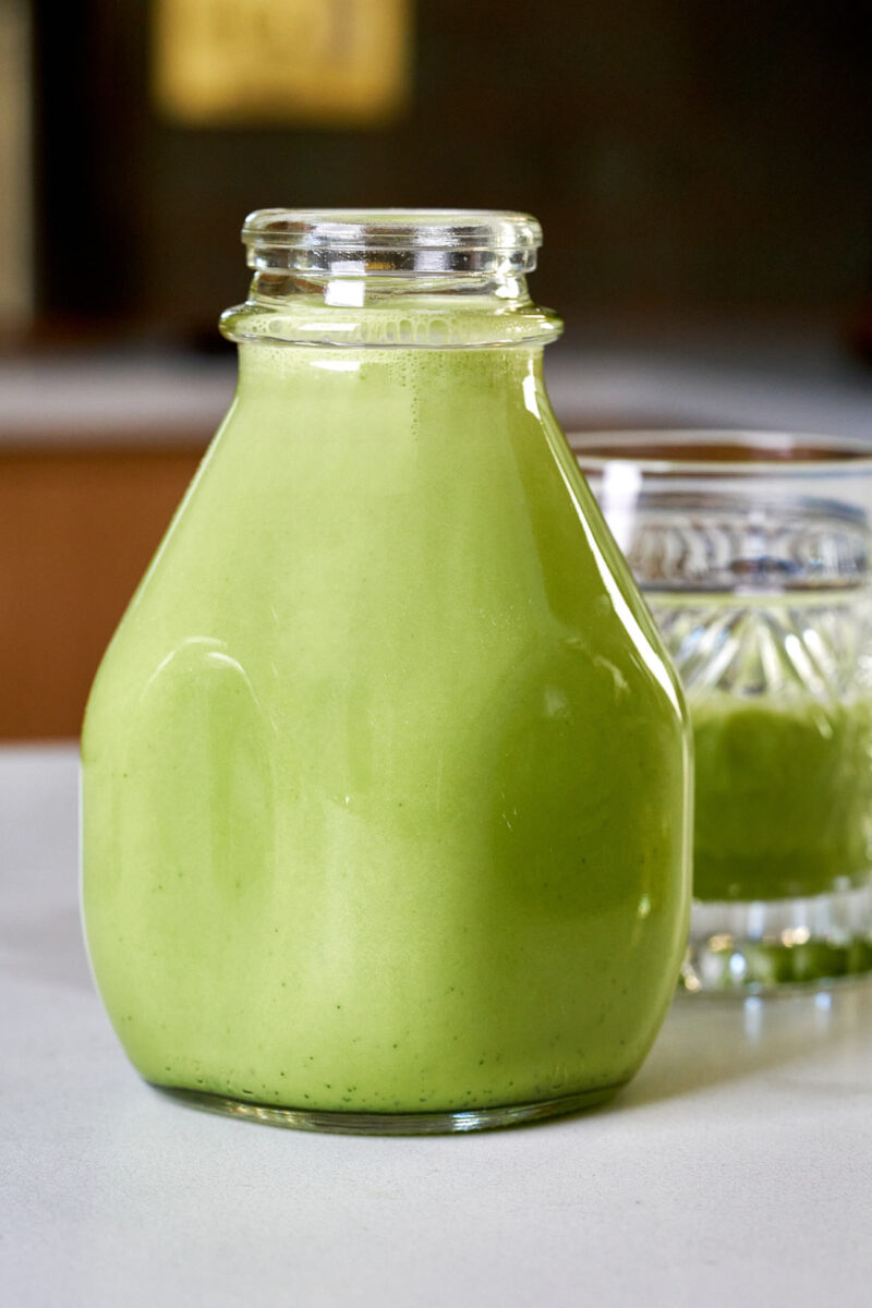 Milk jug filled with Matcha Baileys next to a cocktail.