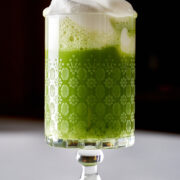 Spiked matcha cocktail with whipped cream in a pedestal glass.