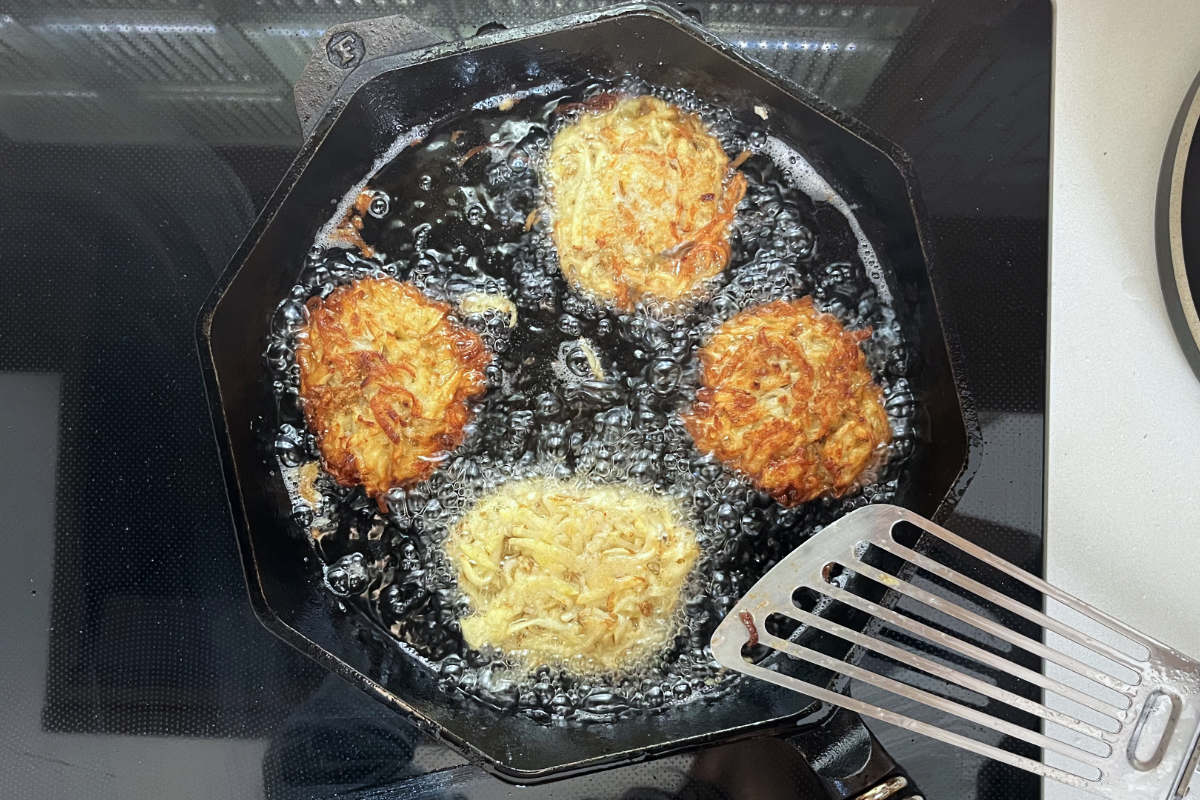 Latkes frying in a cast iron pan.