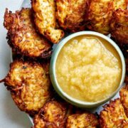 Potato latkes on a platter surrounding a bowl of applesauce.