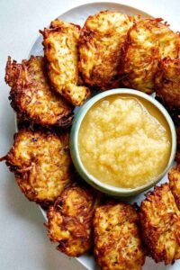 Potato latkes on a platter surrounding a bowl of applesauce.