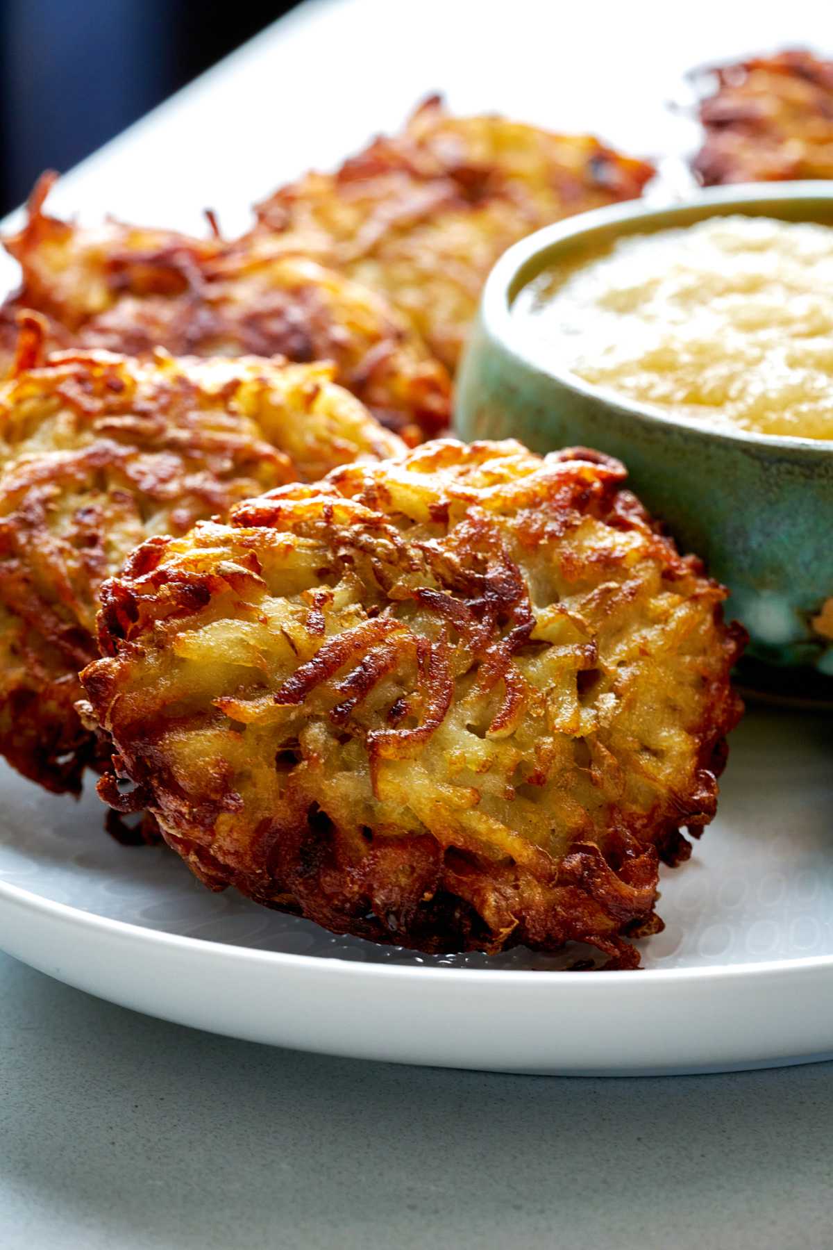 Potato latkes on a platter next to applesauce.