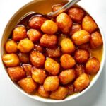 Bamieh soaking in simple syrup in a bowl with a spoon.