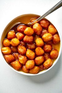 Bamieh soaking in simple syrup in a bowl with a spoon.