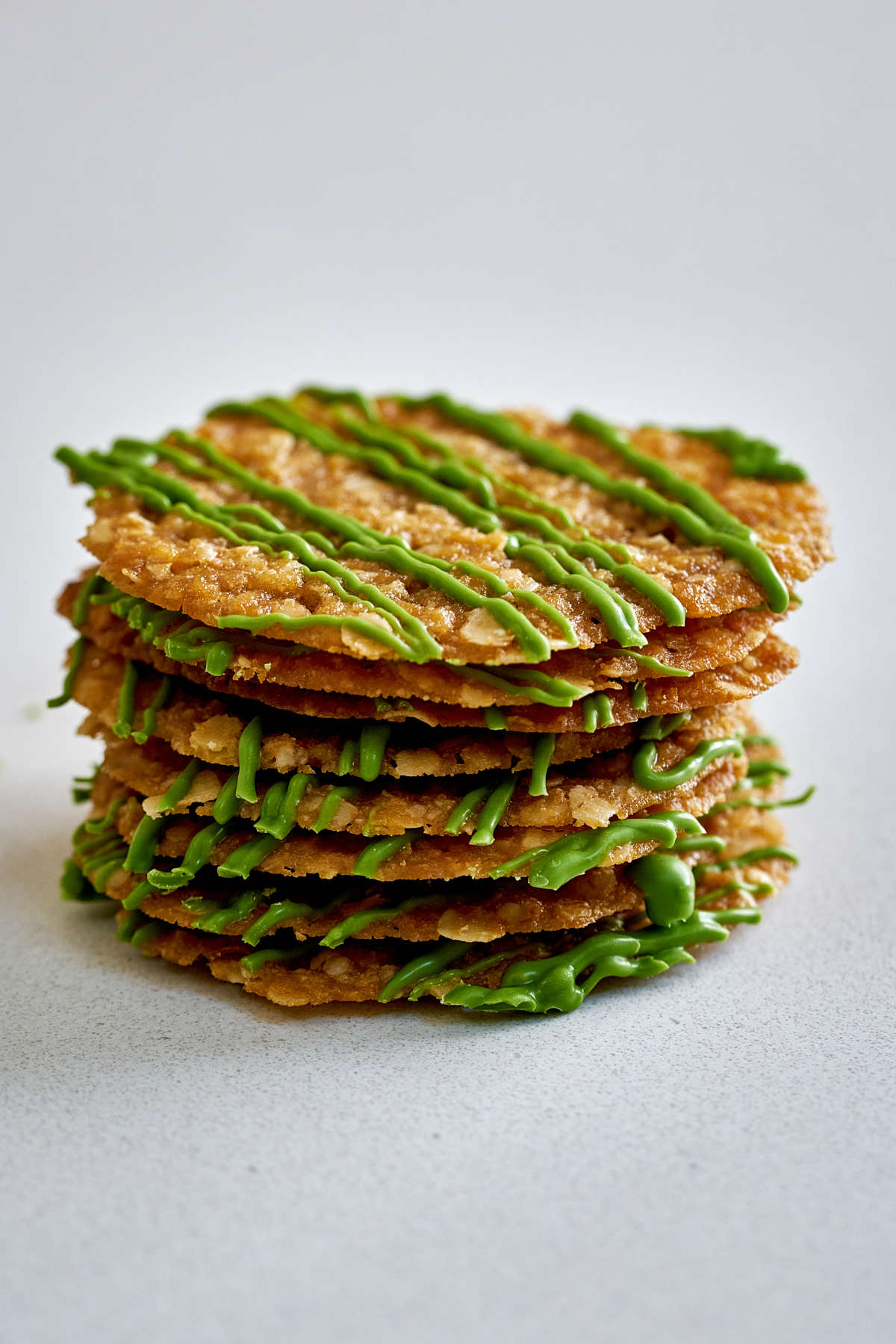 Stack of lace cookies with green chocolate drizzle.