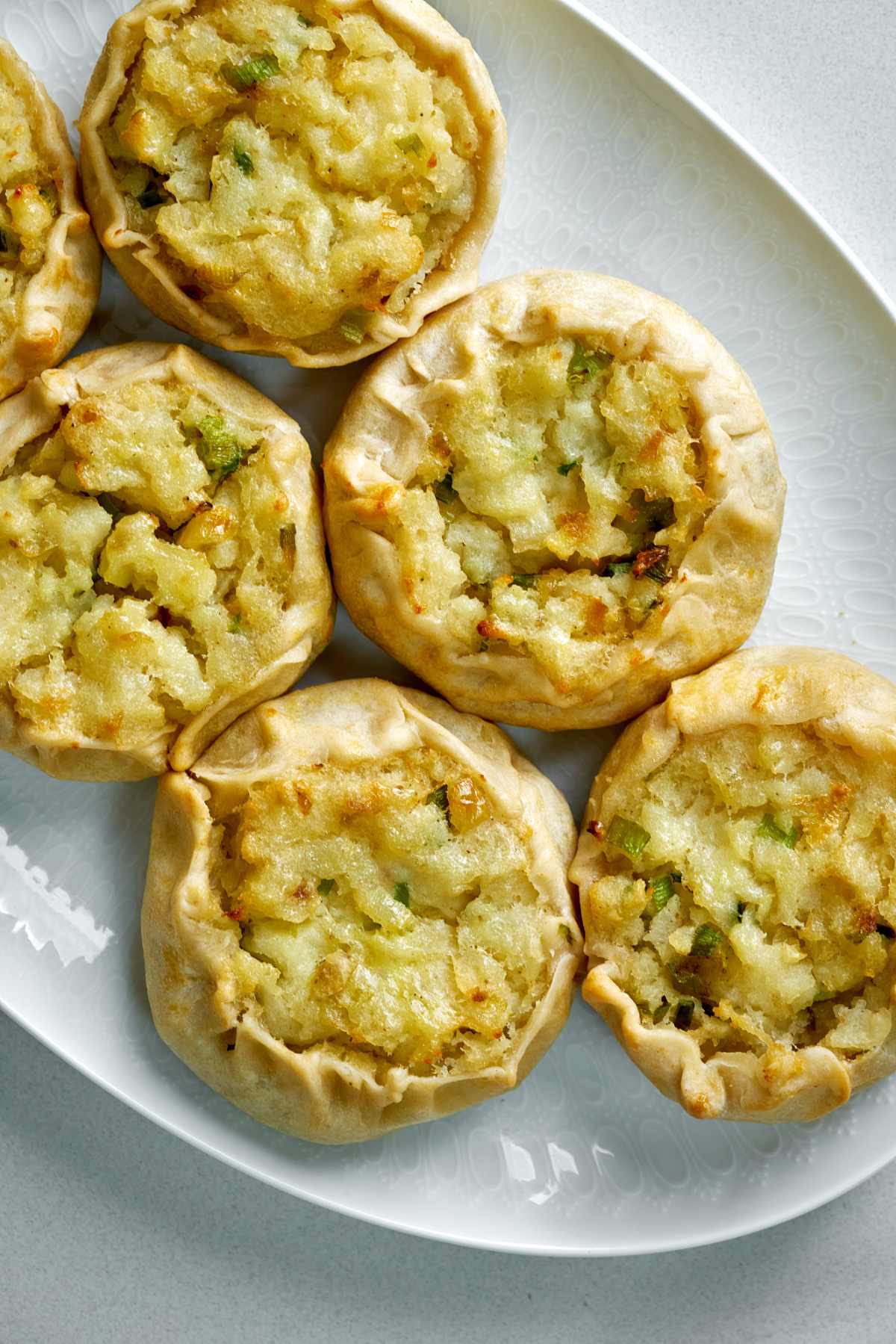 Top view of six potato knishes on an oval plate.