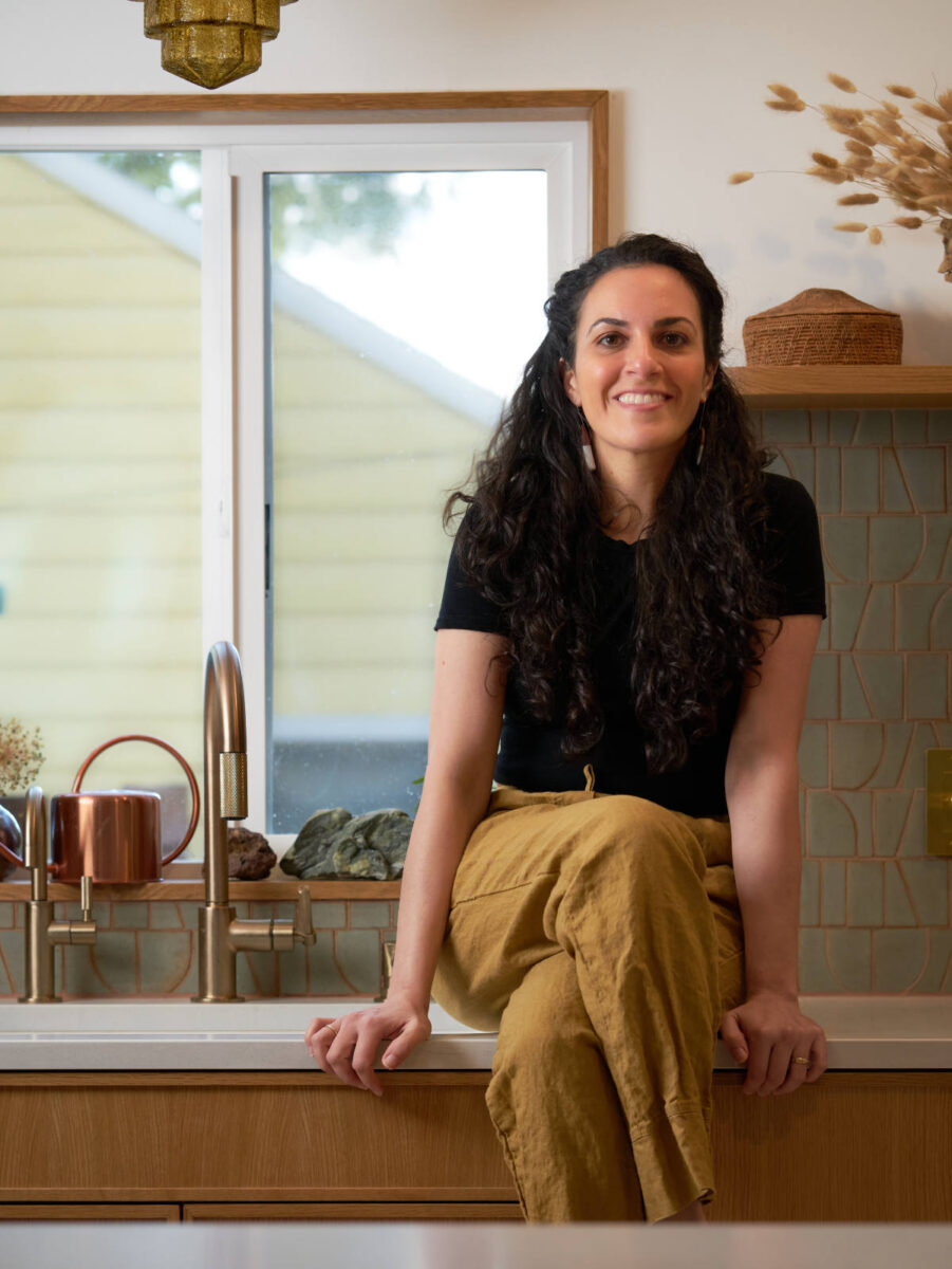 Woman sitting on a kitchen countertop next to a sink.