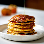Stack of pancakes with syrup drizzling over the top.
