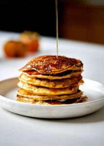 Stack of pancakes with syrup drizzling over the top.