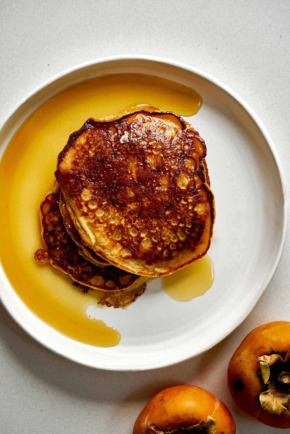 Top view of pancakes in a syrupy plate next to persimmons.