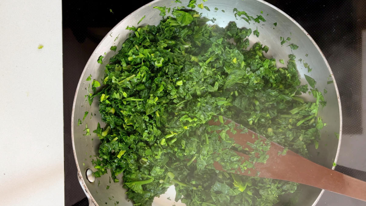 Cooking spinach and herbs in a fry pan.