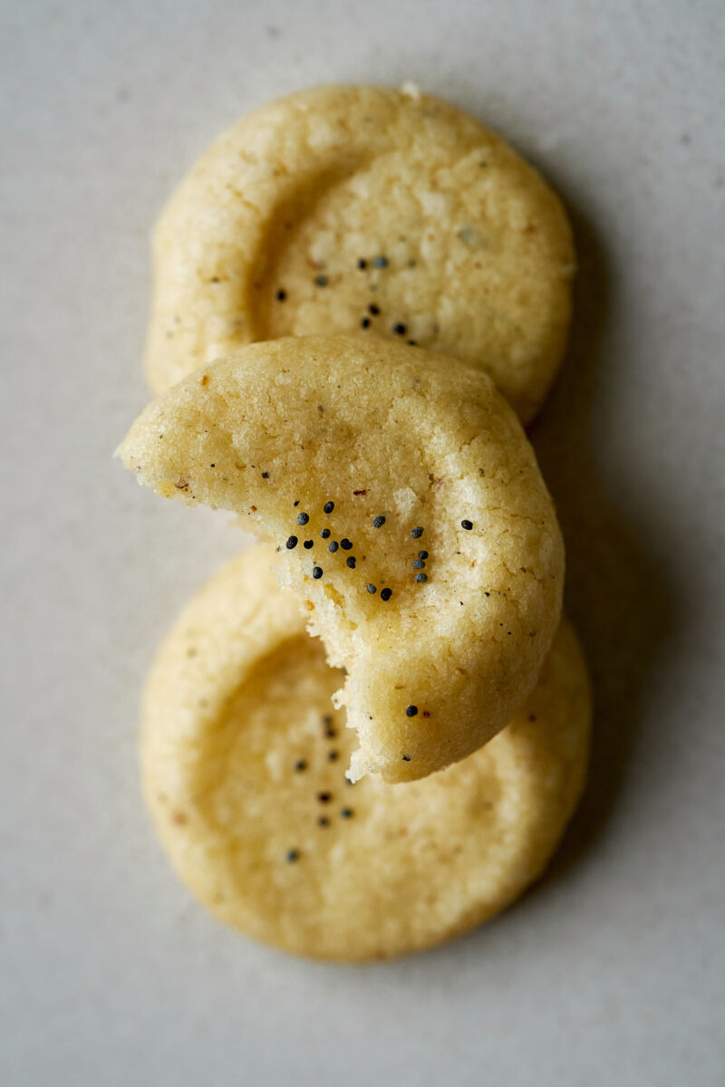 Three cookies with poppy seeds and one with a bite taken out of it.