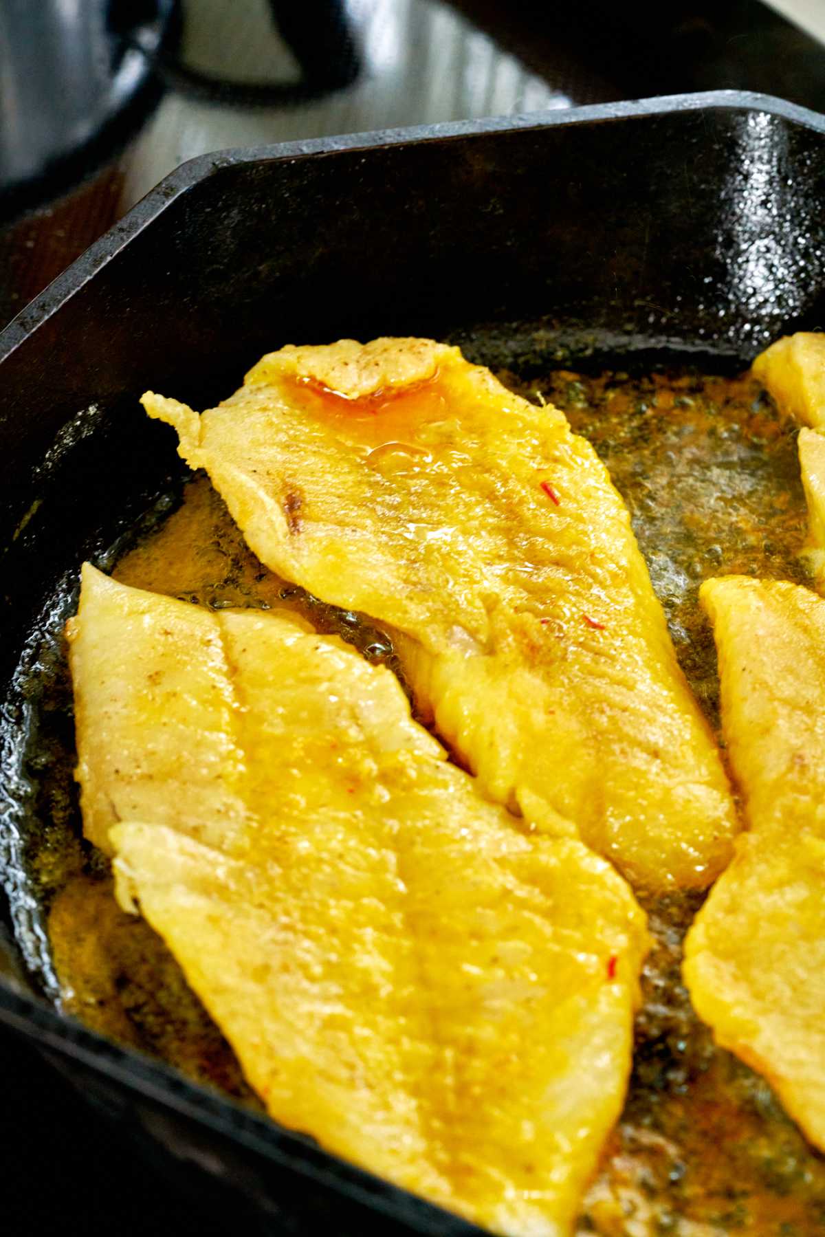 Yellow fish frying in a cast iron pan.