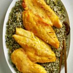 Fried fish on top of green rice.