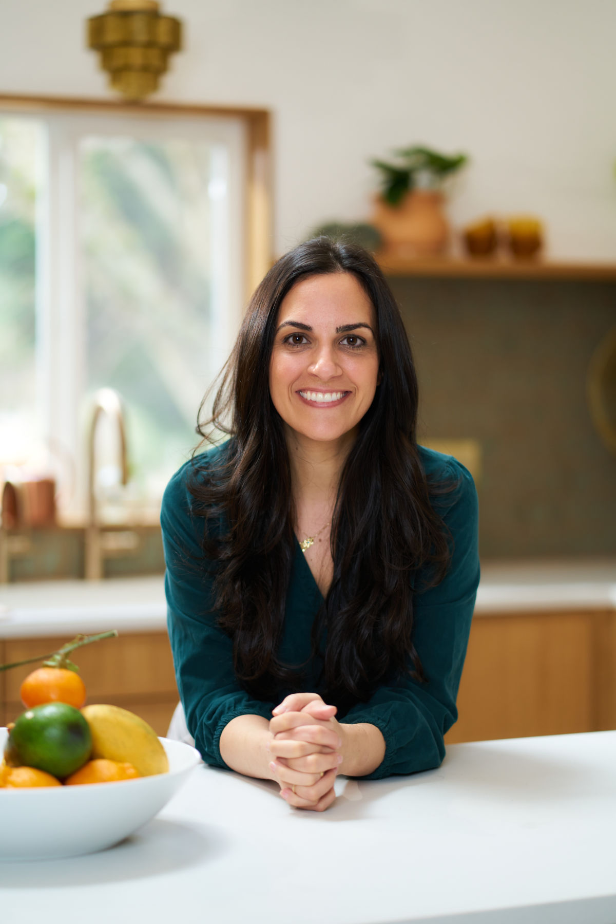 Photo of a woman in a kitchen next to a bowl of fruit.