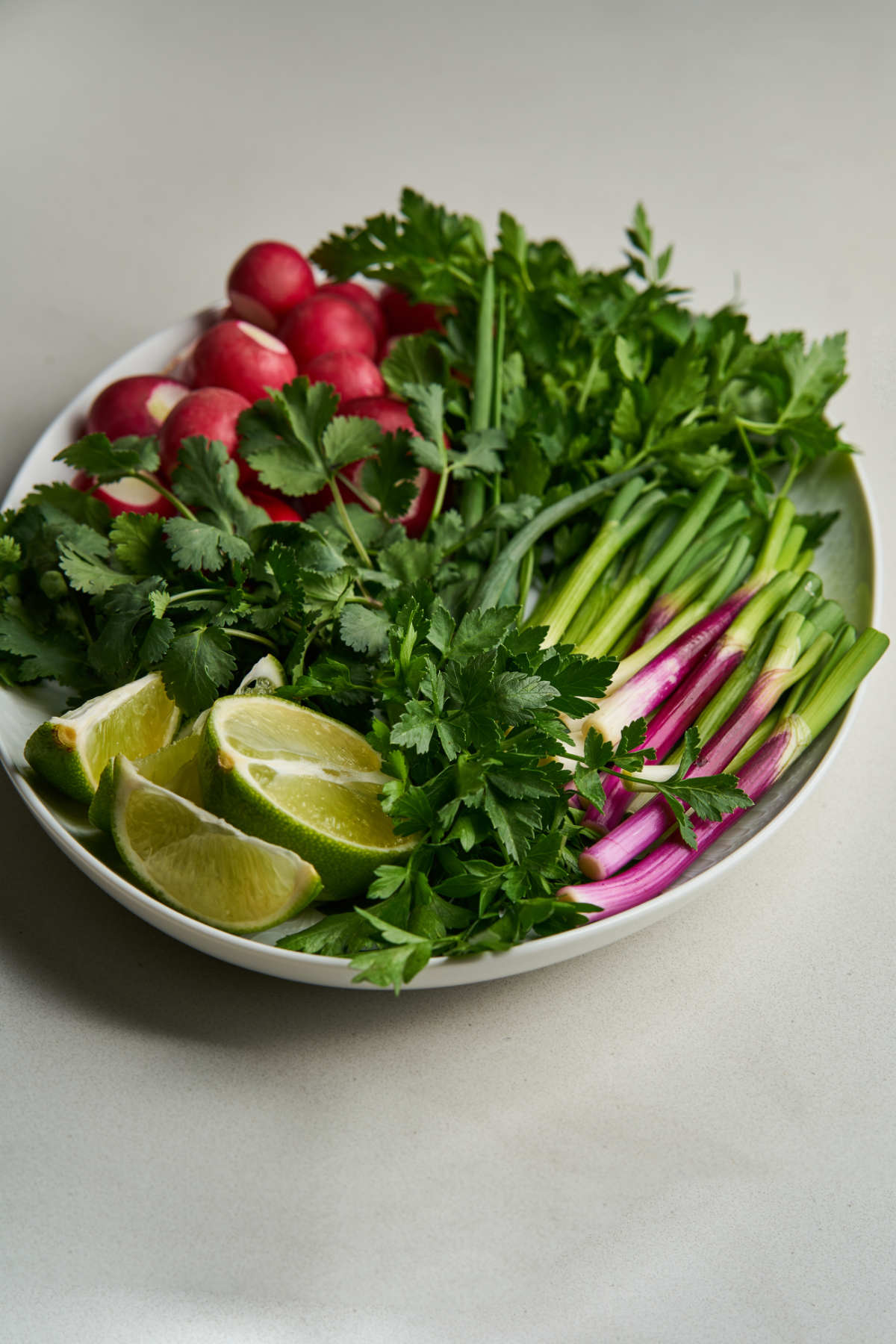 Herbs, scallions, limes, and radishes on a large plate.