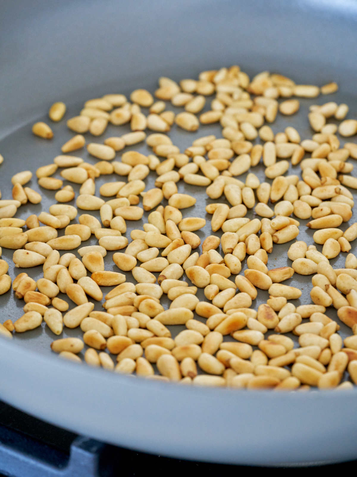 Before and after photos of toasting pine nuts in a pan on the stove.