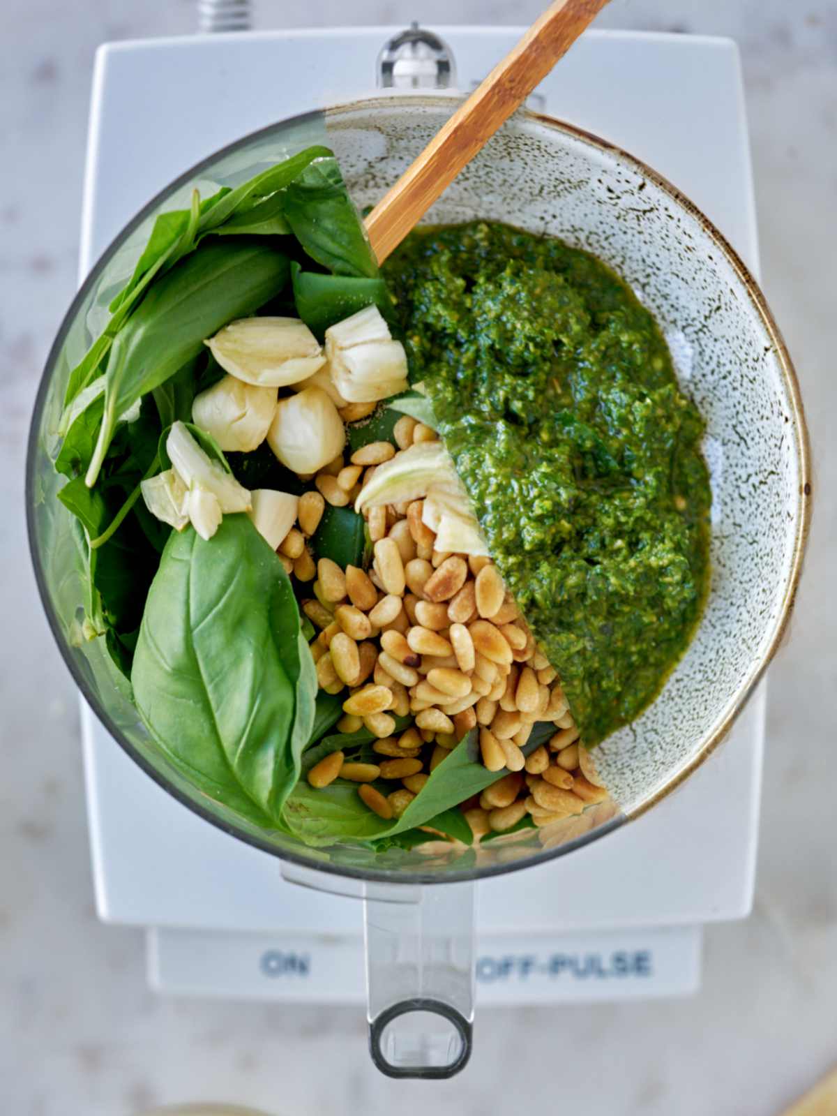 Overhead view of basil, garlic, and pine nuts in a food processor.