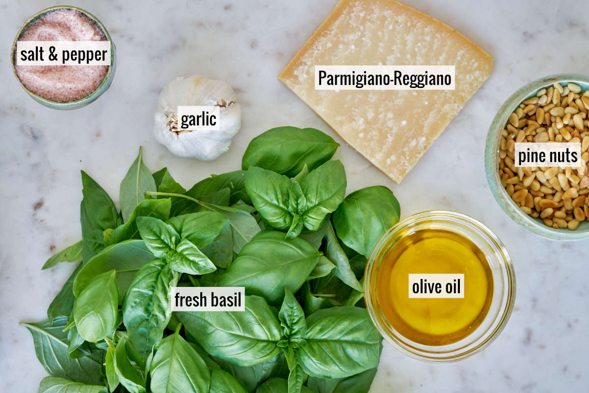 Ingredients for garlic basil pesto on a white marble countertop.