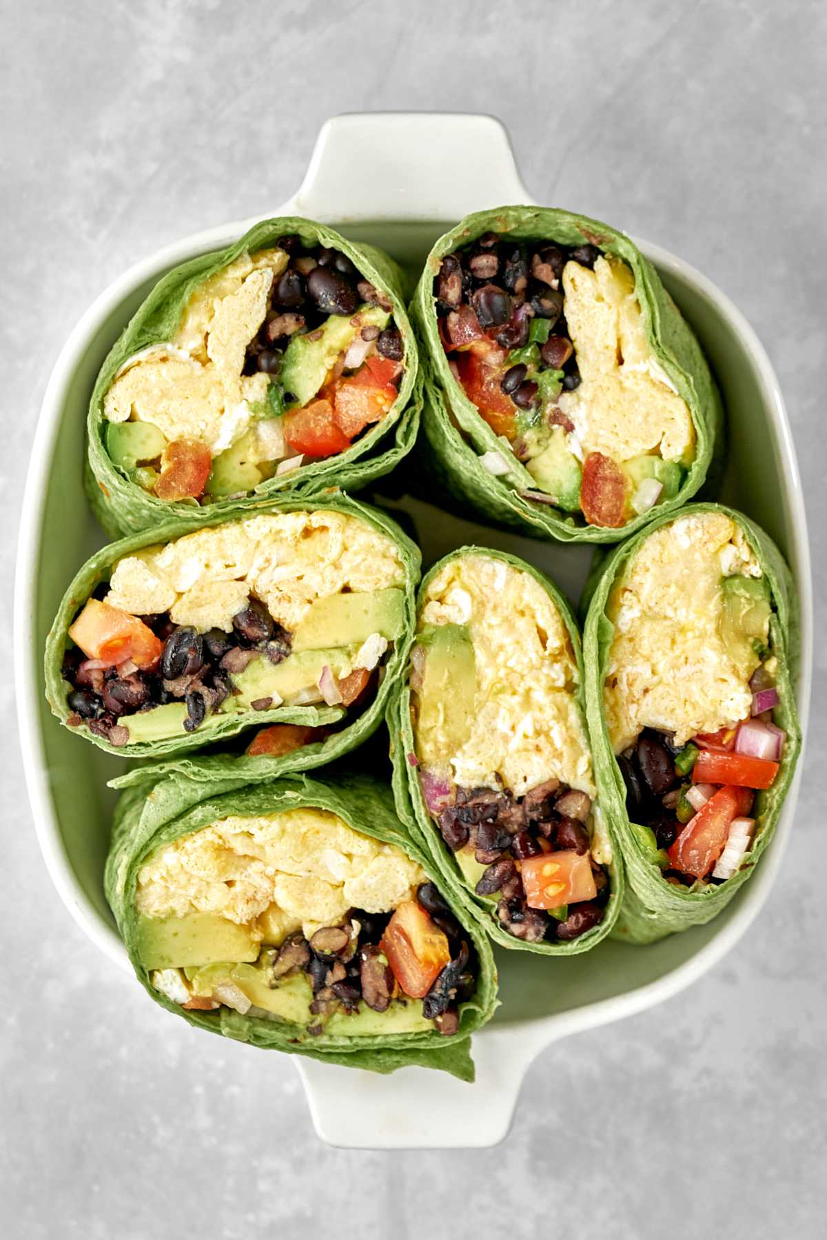 Burritos with green tortillas cut in half so you can see the beans, eggs, and salsa inside in a white dish.