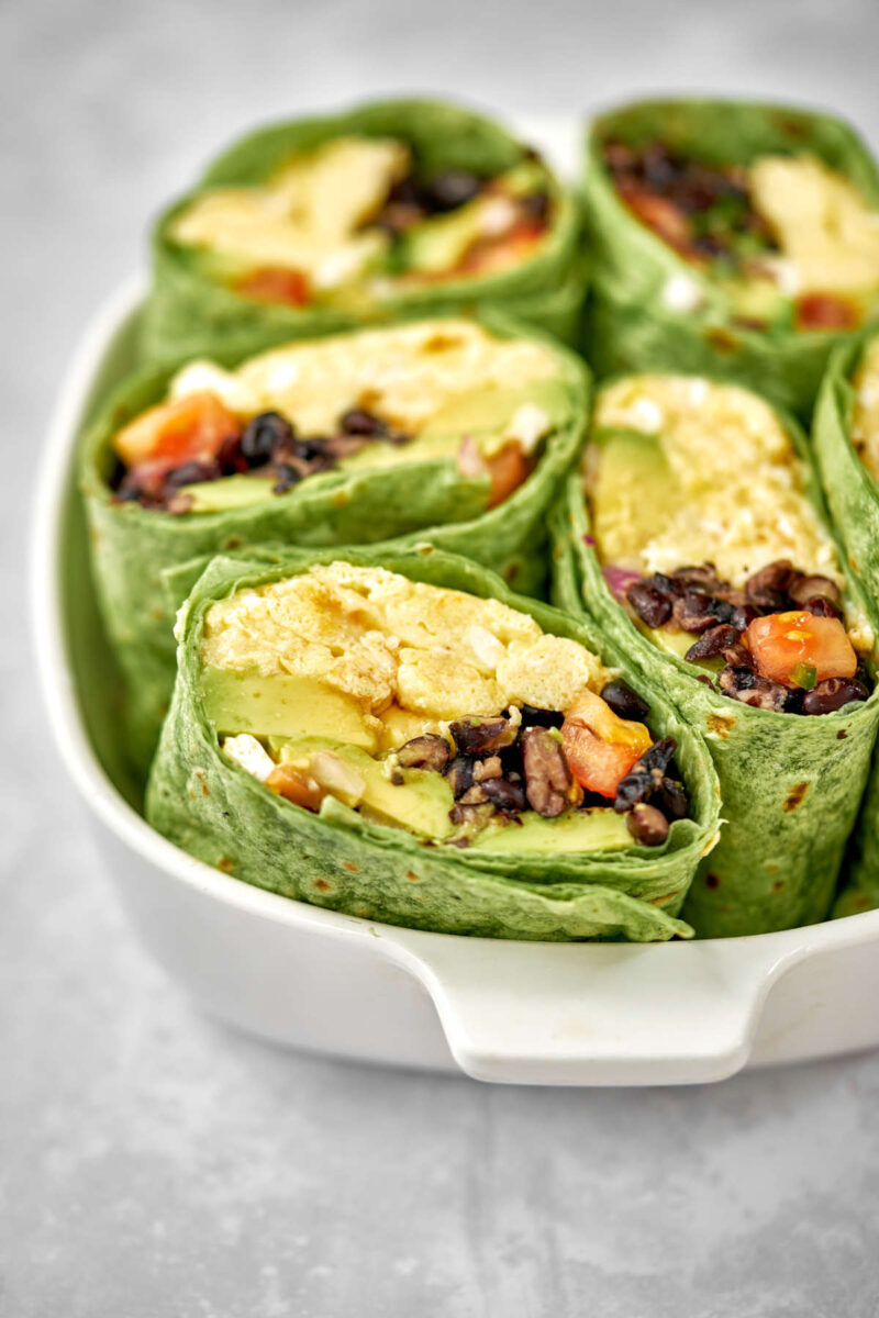 Green burritos cut in half showing the egg and bean filling and nested together in a white dish.