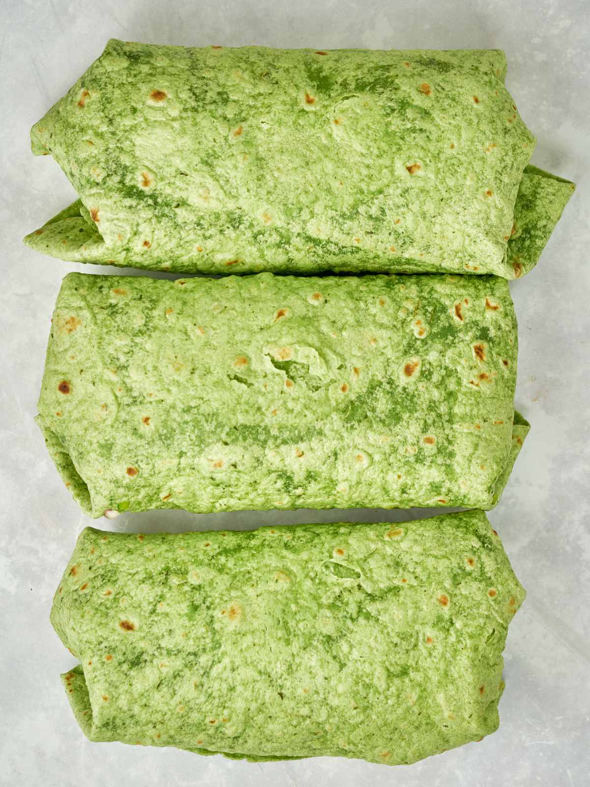 Three green burritos stacked next to each other.