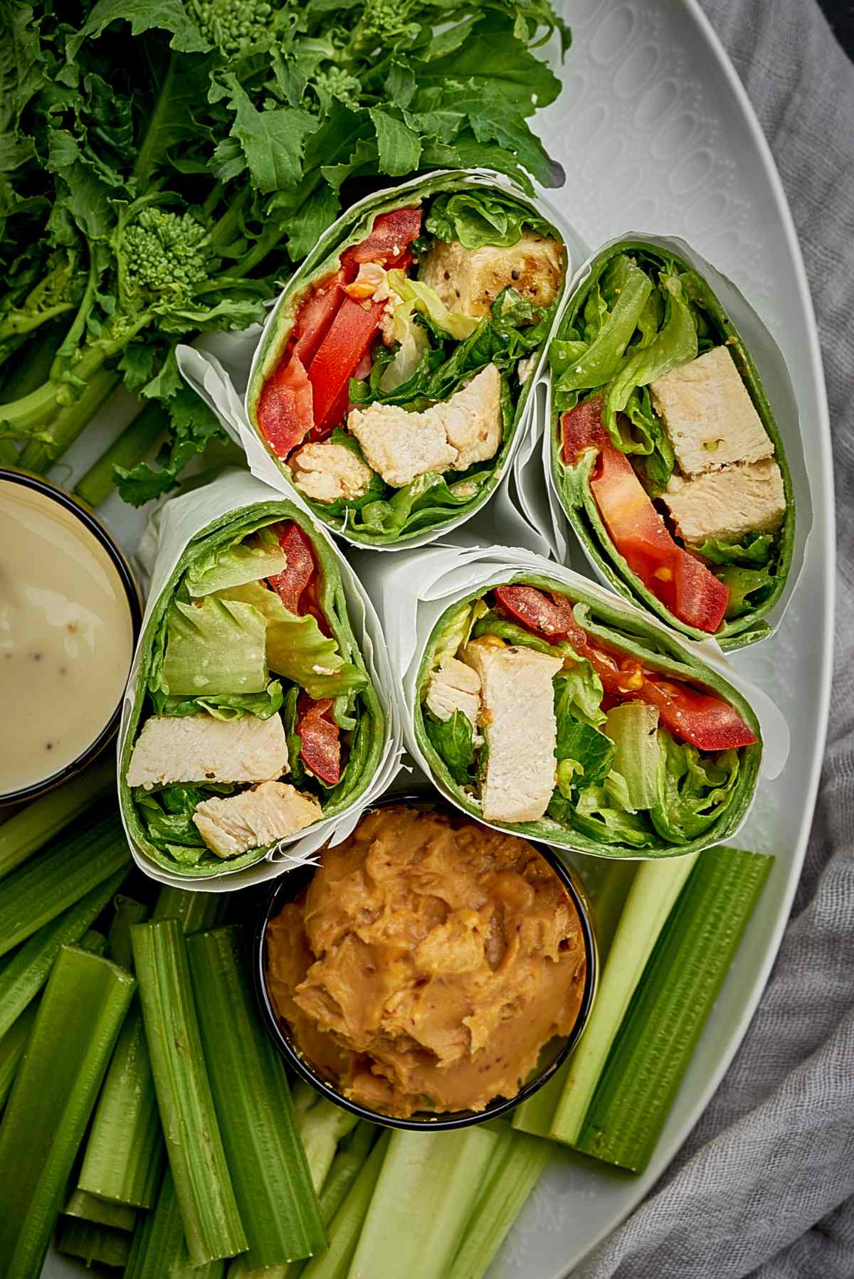 Caesar salad wraps with chunks of chicken and tomatoes on a platter with celery and peanut butter.
