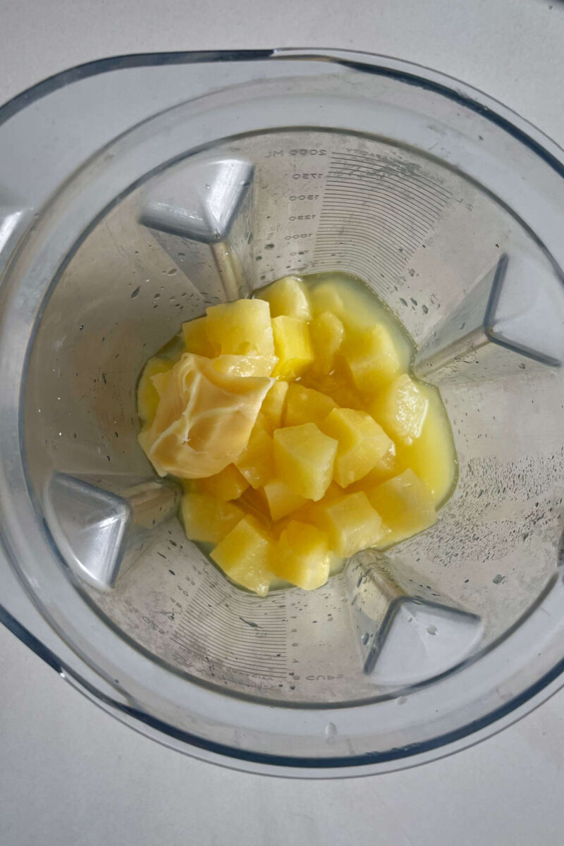 Pineapple chunks in a blender with some pineapple juice and sweetened condensed coconut milk.