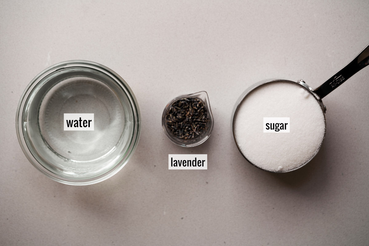 Sugar, lavender flowers, and water in separate containers on a countertop.