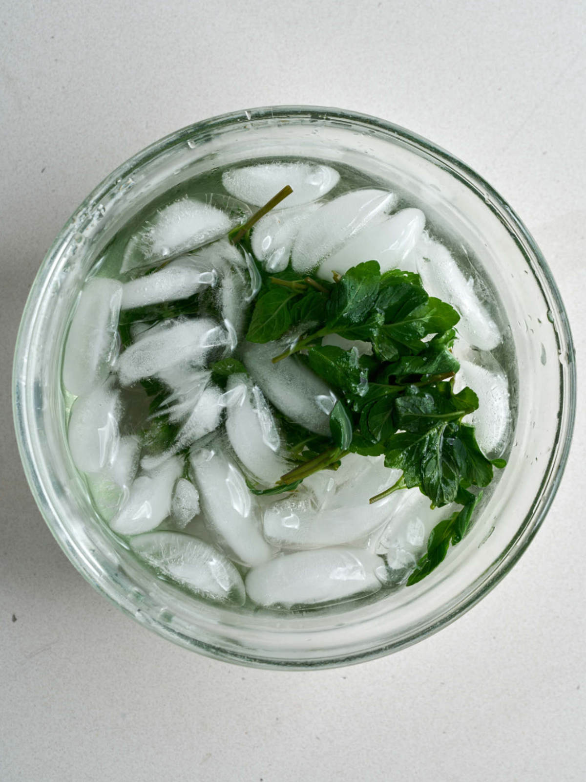 Blanched greens in an ice bath in a glass bowl.