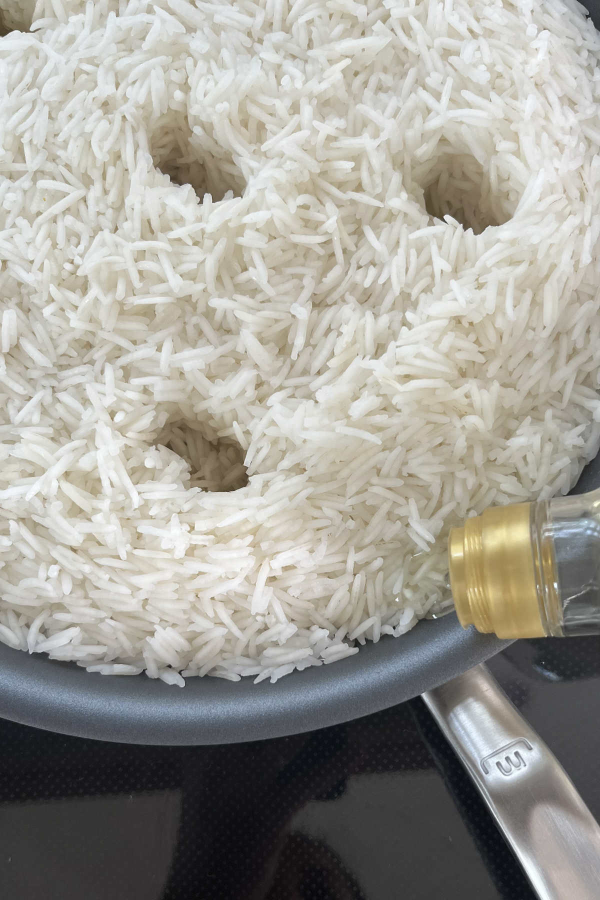 Pouring oil over rice in a fry pan with holes.