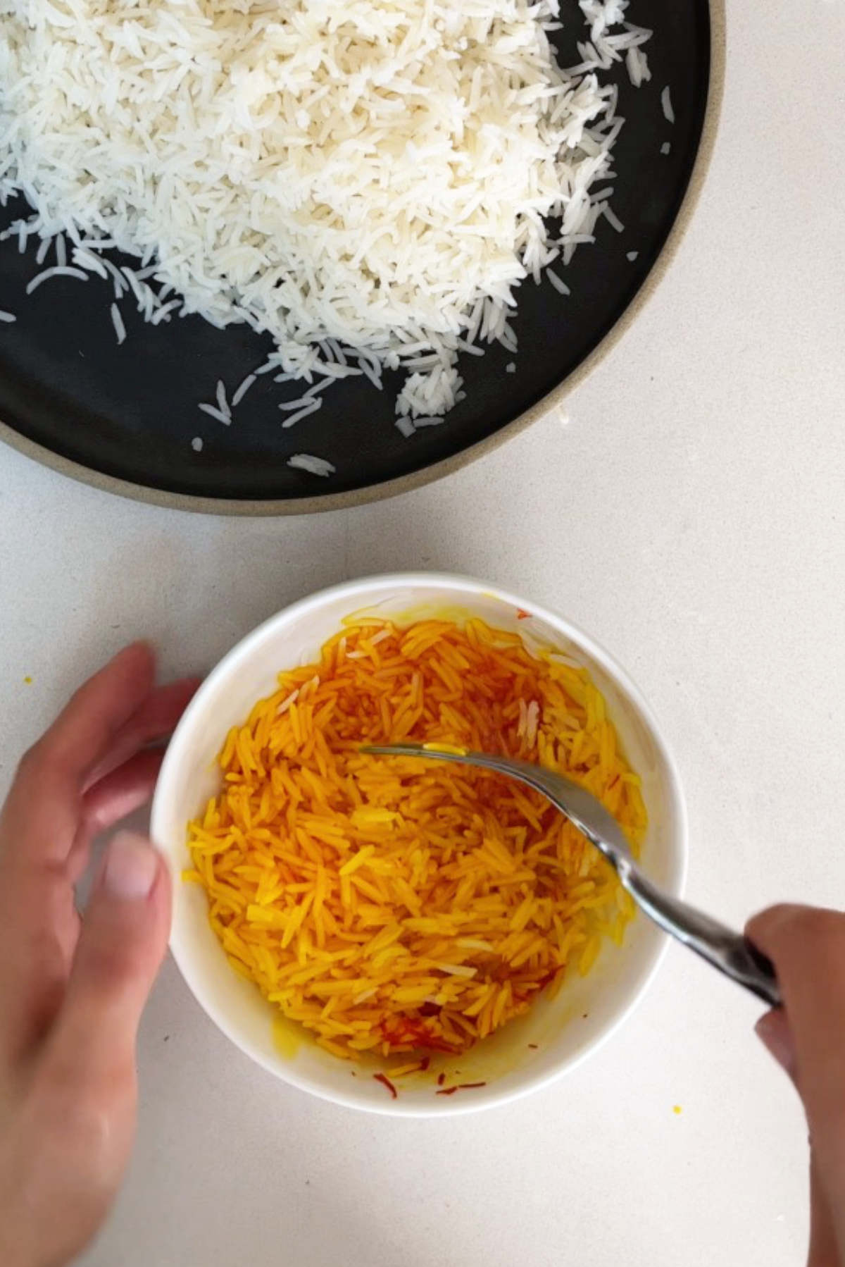 Yellow saffron rice in a small bowl next to white rice on a black platter.