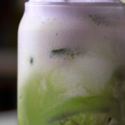 Close up of a matcha latte in a class with purple foam on top.