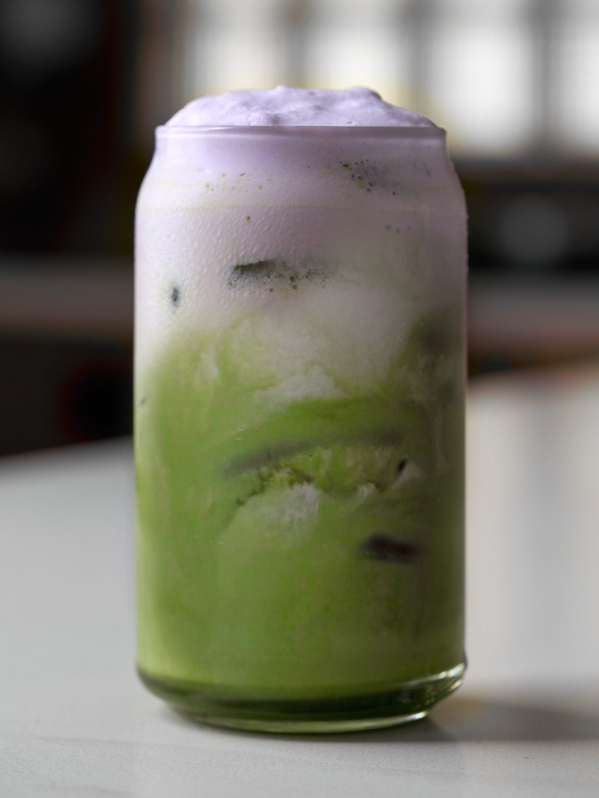 Green and purple iced latte in a glass on a countertop.