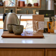 Tea kettle, cups, and glass pitchers set up on a countertop with different bags of tea behind them.