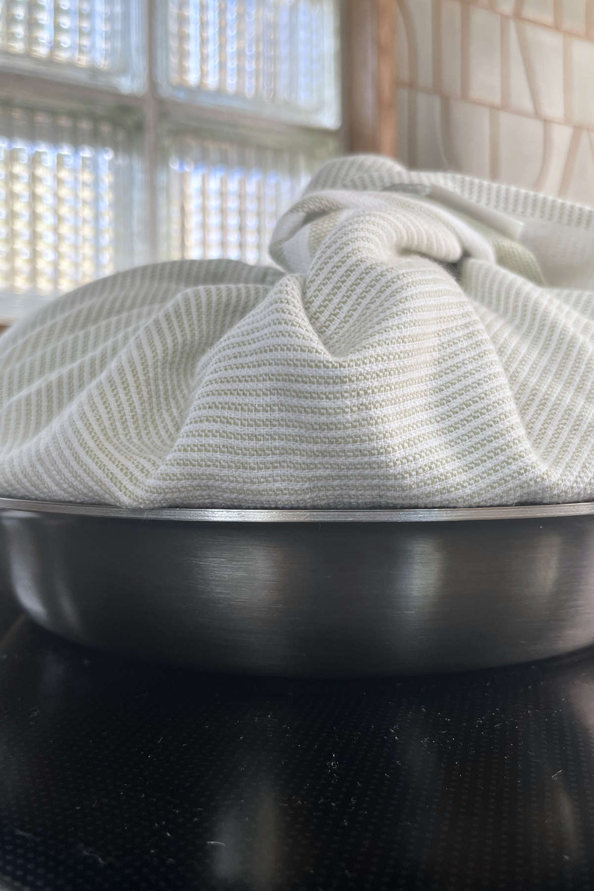 Fry pan topped with a lid that is wrapped in a clean kitchen towel.
