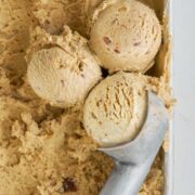 Three scoops of ice cream and an ice cream scooper on top of a bin of ice cream.