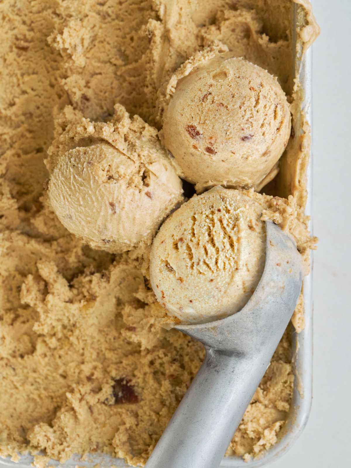 Three scoops of ice cream and an ice cream scooper on top of a bin of ice cream.