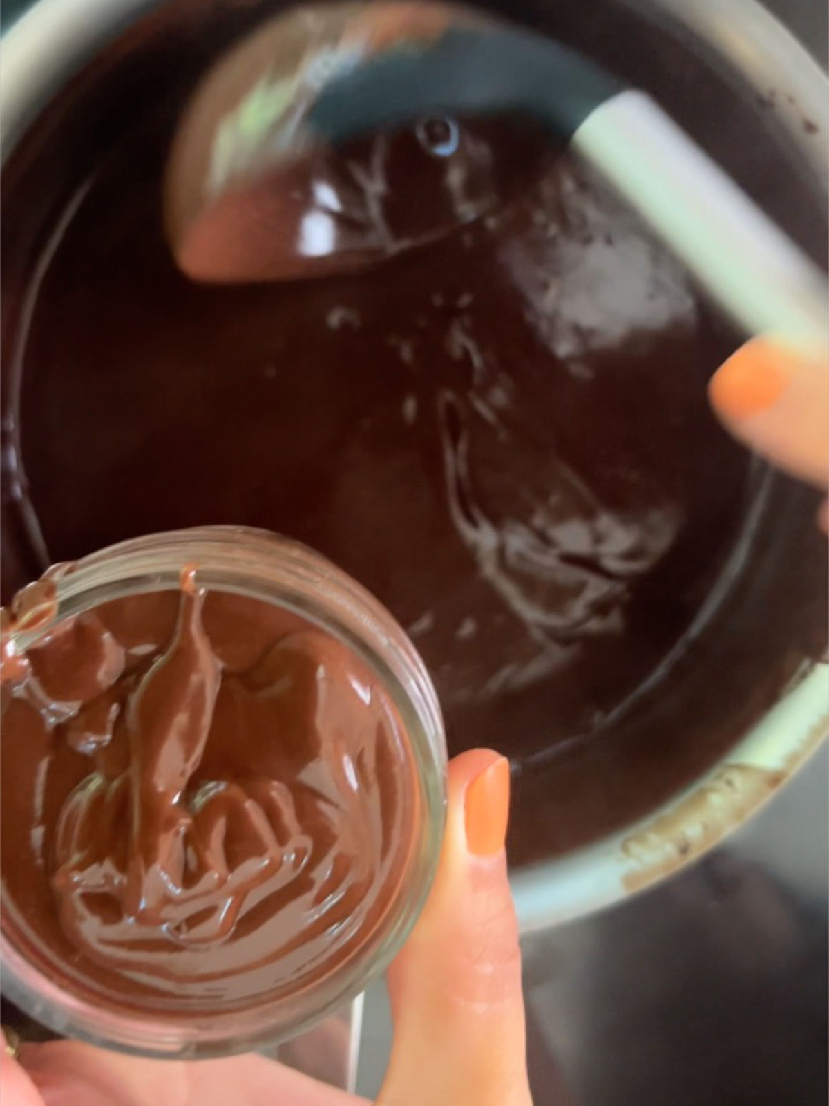 One hand scooping pudding from a metal pot with a ladle and another hand holding a small jar filled with pudding.