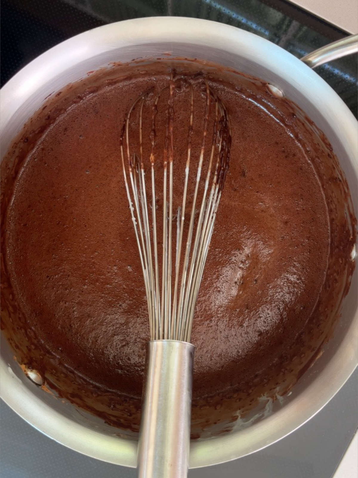 Chocolate liquid in a metal pot with a metal whisk.