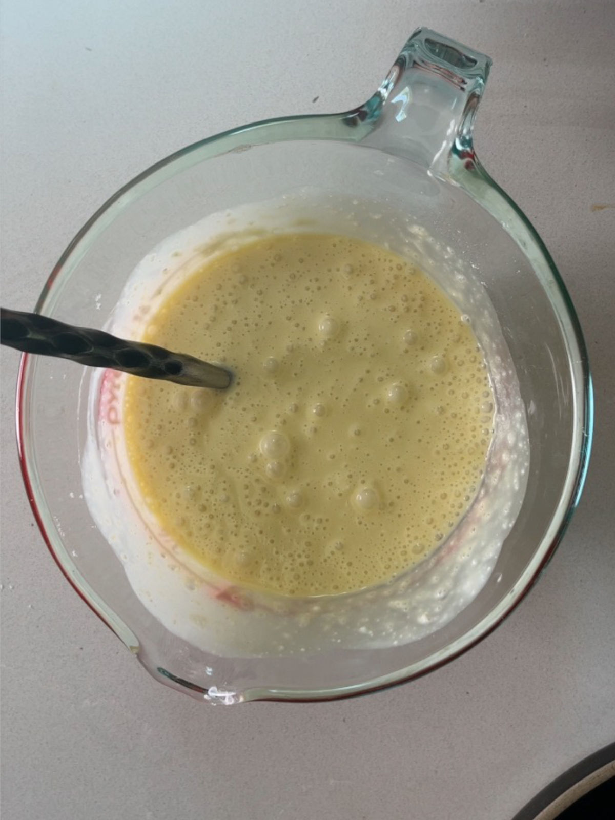 Pale yellow liquid in a glass measuring cup with a metal utensil in it.