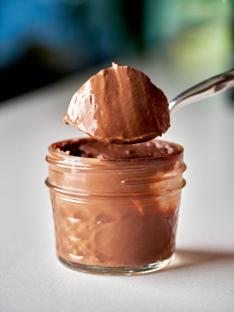 Chocolate pudding in a small glass jar with a large spoonful of pudding held over the jar.