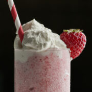 Pink milkshake with a whipped cream topping, strawberry, and red and white striped straw.